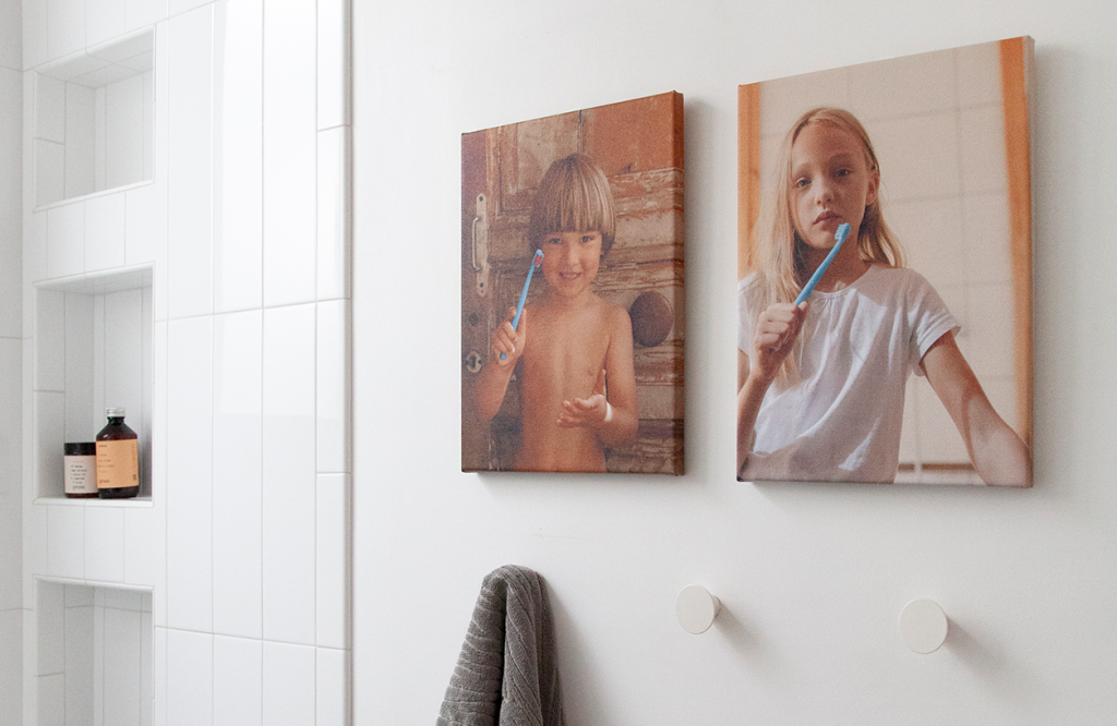 Canvases of two children hung on the wall of a bathroom