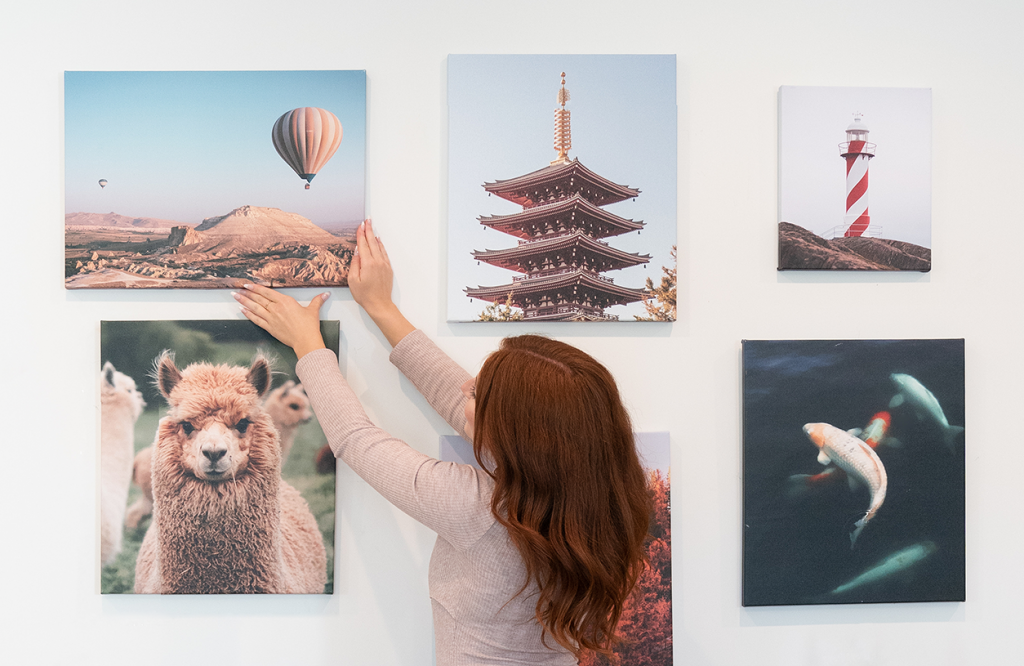 Woman hangs canvas print on a wall with other various sized canvases